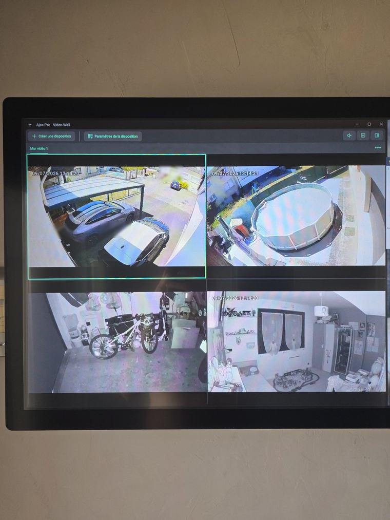 Écran mural affichant quatre caméras de vidéosurveillance : allée, piscine, garage et intérieur d'une maison à Nancy
